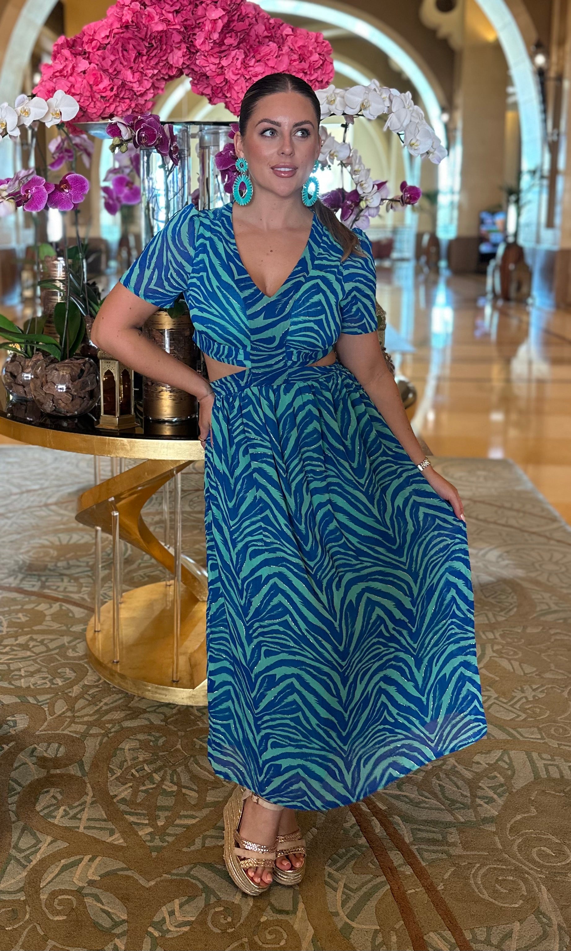 Woman in a blue dress sitting in a luxurious interior setting with floral decorations.