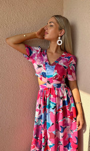 Woman wearing a colorful floral dress against a beige wall